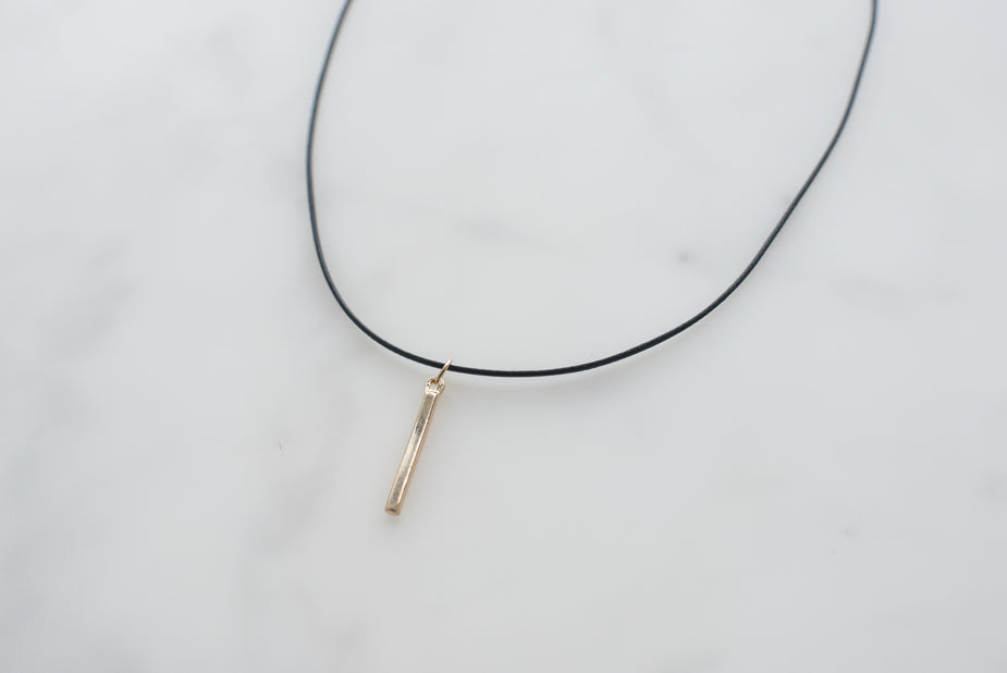 Black cord choker necklace with minimalist gold bar pendant on white background