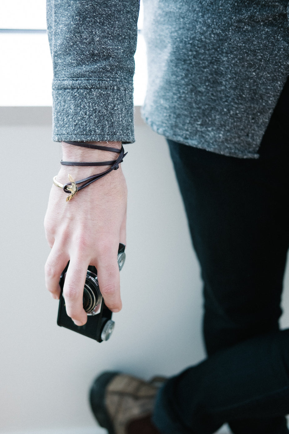 Mens anchor bracelet with black leather straps and gold hook clasp worn on wrist with blue blazer