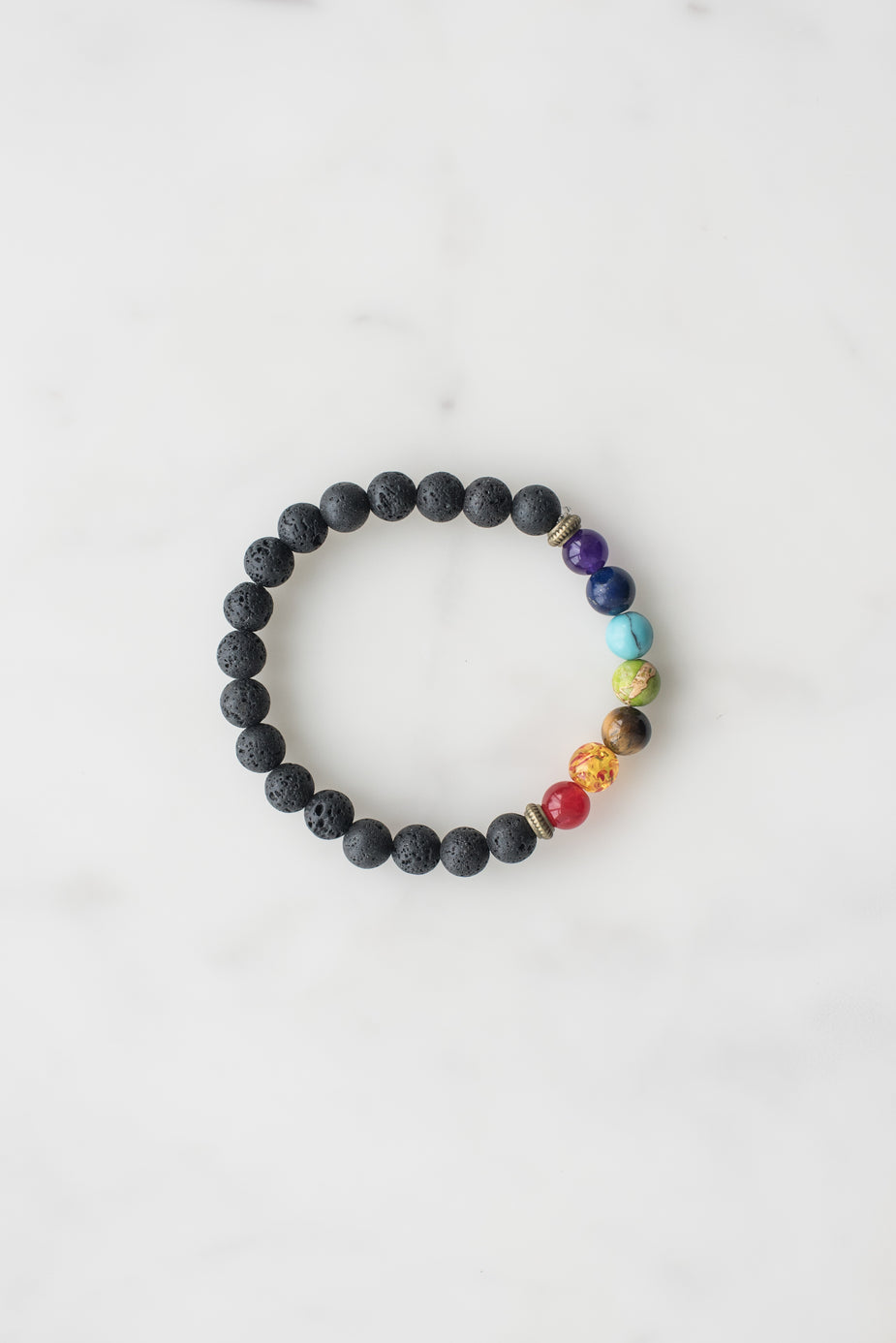 7 Chakra Bracelet with black lava beads and colorful gemstones representing each chakra on white background.