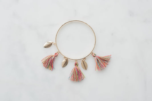 Boho bangle bracelet with colorful tassel charms and gold leaf accents on marble background.