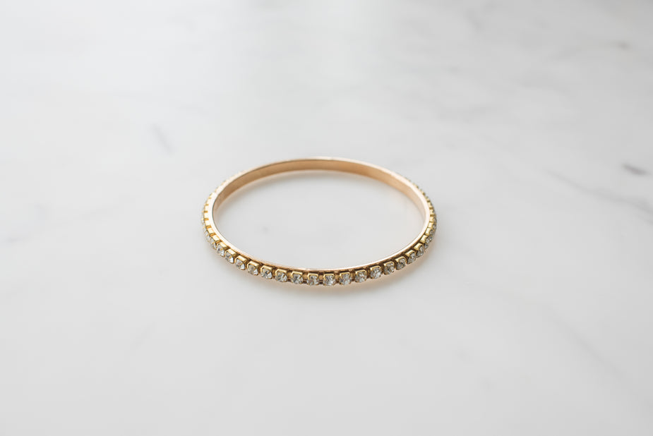 Gold bangle bracelet with sparkling crystal stones set around the entire circumference on marble surface.