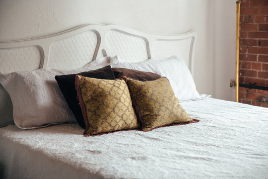 Brown throw pillows with gold pattern displayed on white bed with decorative headboard