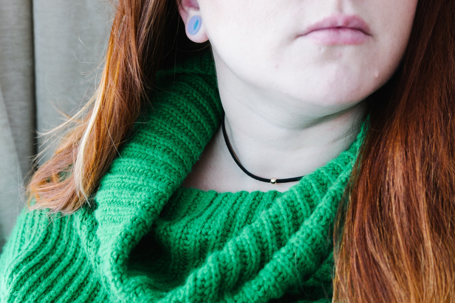 Black choker with bead worn by person with red hair and green sweater