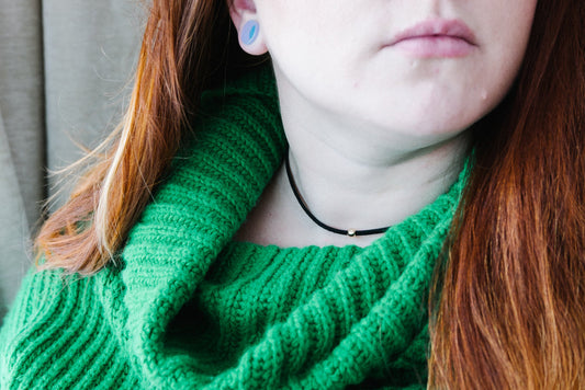 Black choker with bead worn by person with red hair and green sweater