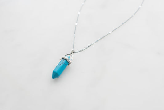Turquoise gemstone necklace with silver-plated pendant on delicate chain, blue crystal point jewelry.