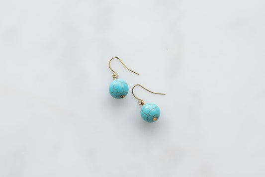 Turquoise boho earrings with gold hooks on white background, featuring round beads with veining detail.