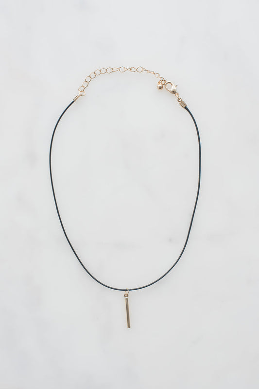 Black leather choker necklace with gold chain extender, lobster clasp, and small gold bar pendant on white background.