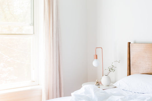 Copper light pendant with white globe shade hanging above wooden bed nightstand with white bedding
