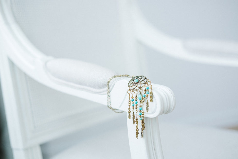 Dreamcatcher pendant necklace with turquoise beads and gold chain fringe displayed on white fabric backdrop