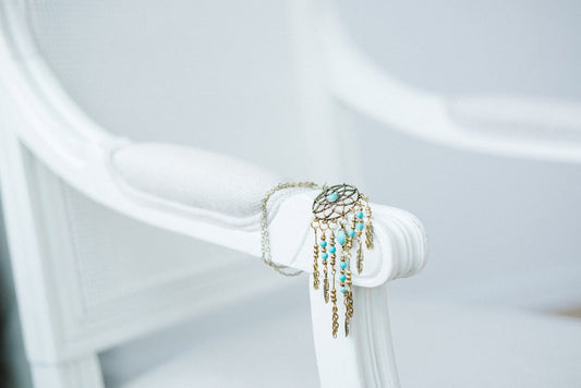 Dreamcatcher pendant necklace with turquoise beads and gold chain fringe displayed on white fabric backdrop