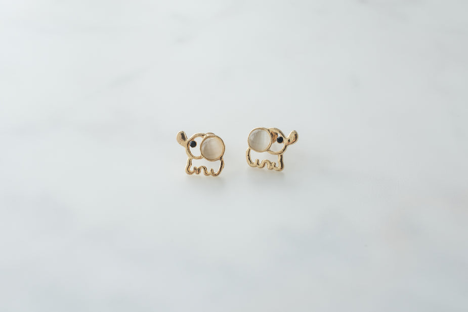 Gold elephant stud earrings with white stone eyes on white background, cute animal jewelry pair.