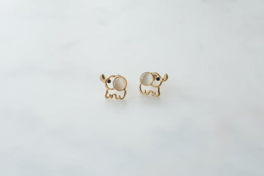 Gold elephant stud earrings with white stone eyes on white background, cute animal jewelry pair.