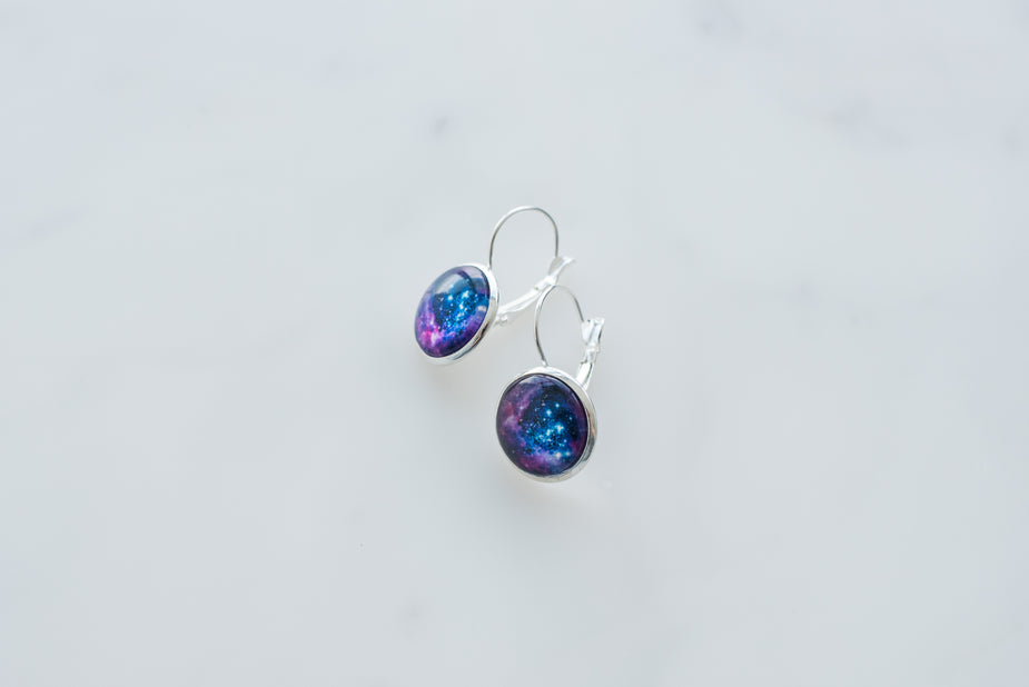 Galaxy Earrings with blue and purple cosmic design in silver settings on white background.