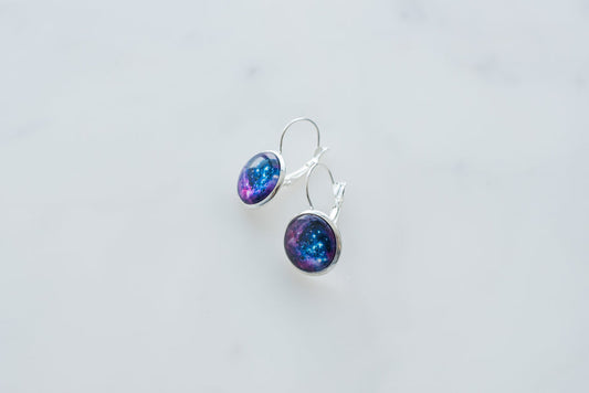 Galaxy Earrings with blue and purple cosmic design in silver settings on white background.