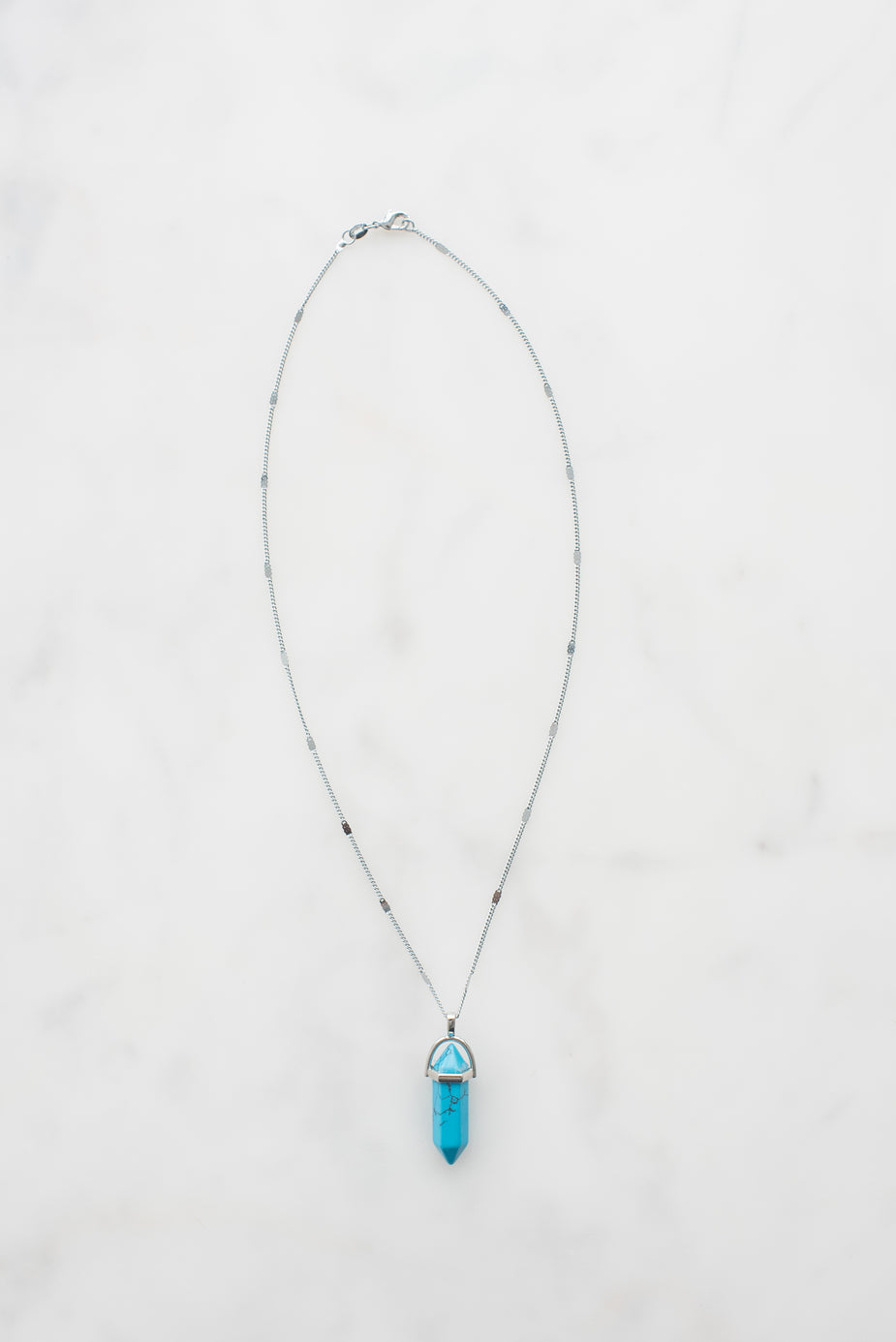 Turquoise gemstone necklace with silver chain and metal cap pendant on white background.