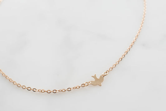 Gold bird necklace with delicate chain on white background, elegant minimalist jewelry design.
