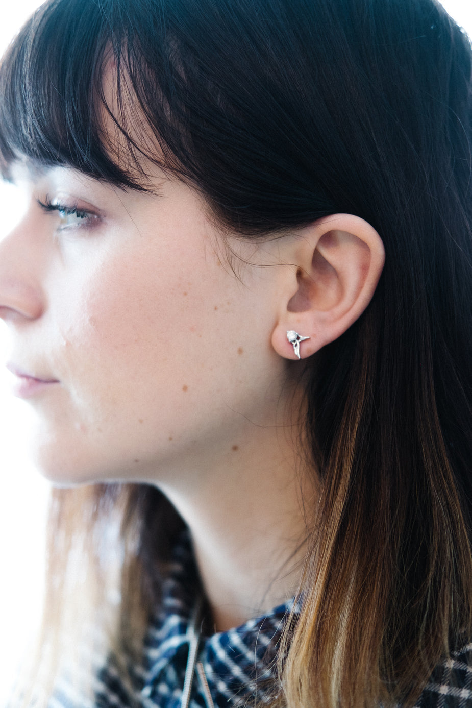 Guardian Angel Earrings silver studs worn by woman with dark hair and bangs, side profile view
