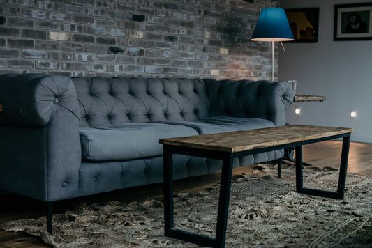 Grey tufted sofa with rolled arms in modern living room with wooden coffee table and blue lamp