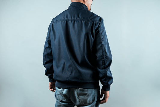 Man wearing navy sports jacket with ribbed cuffs and collar, paired with blue denim jeans, shown from back view.