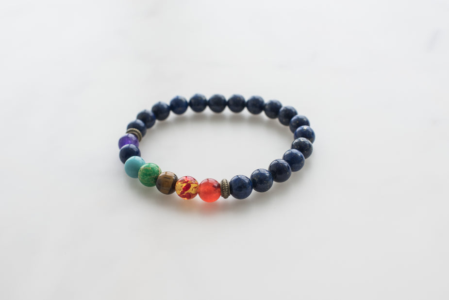 7 Chakra Bracelet with colorful beads including dark blue lapis lazuli, purple, green, tiger's eye, and red carnelian stones.