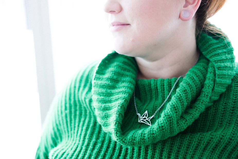 Silver origami crane necklace worn on green sweater, delicate pendant jewelry