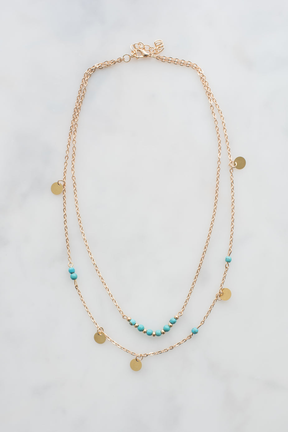 Gold layered necklace with turquoise beads and gold disc charms on adjustable chain.