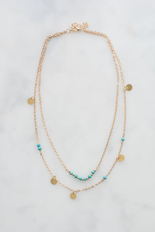 Gold layered necklace with turquoise beads and gold disc charms on adjustable chain.