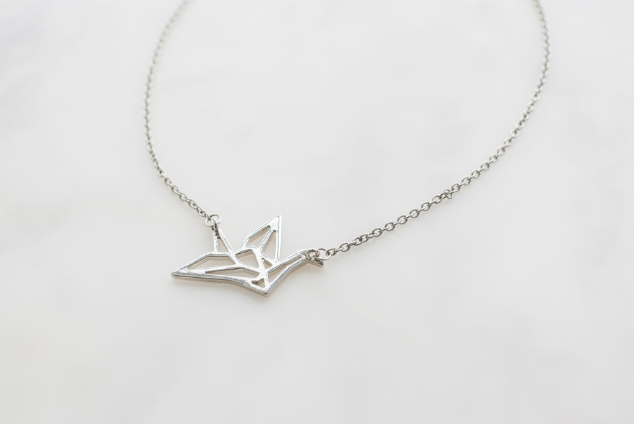 Silver origami crane necklace pendant on delicate chain against white background