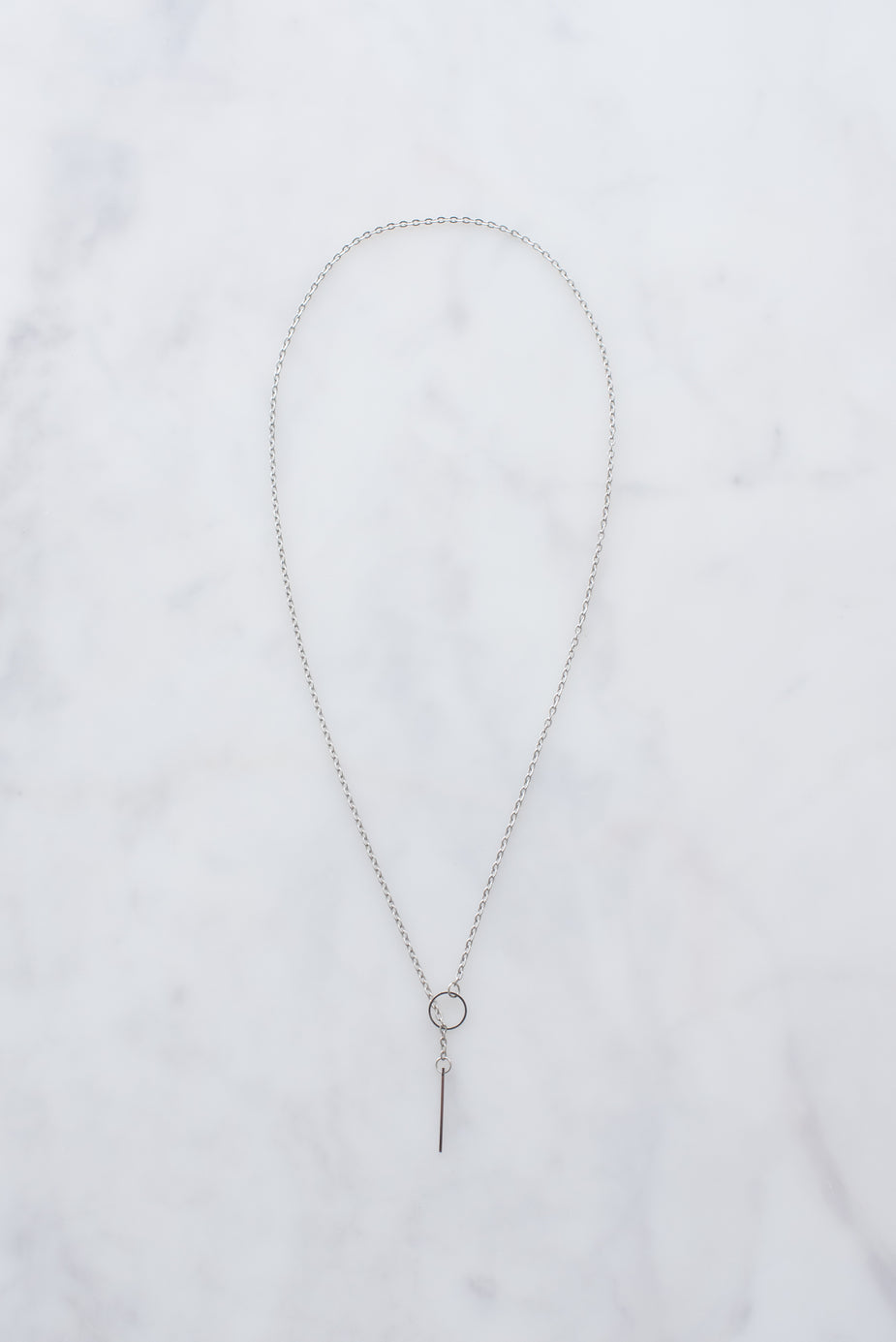 Silver threader necklace with delicate chain and hanging bar pendant on white marble background.