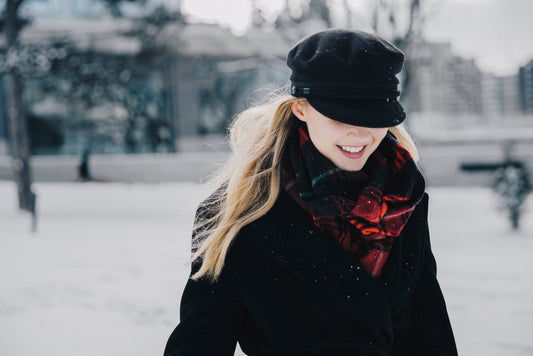 Woman wearing black soft winter jacket with red plaid scarf and black cap in snowy outdoor setting.