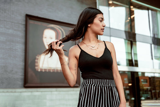 Woman wearing black camisole top with black and white striped skirt, standing outdoors near modern building