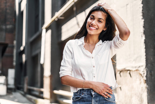 Woman wearing white cotton shirt and jeans, smiling outdoors in natural sunlight against urban backdrop