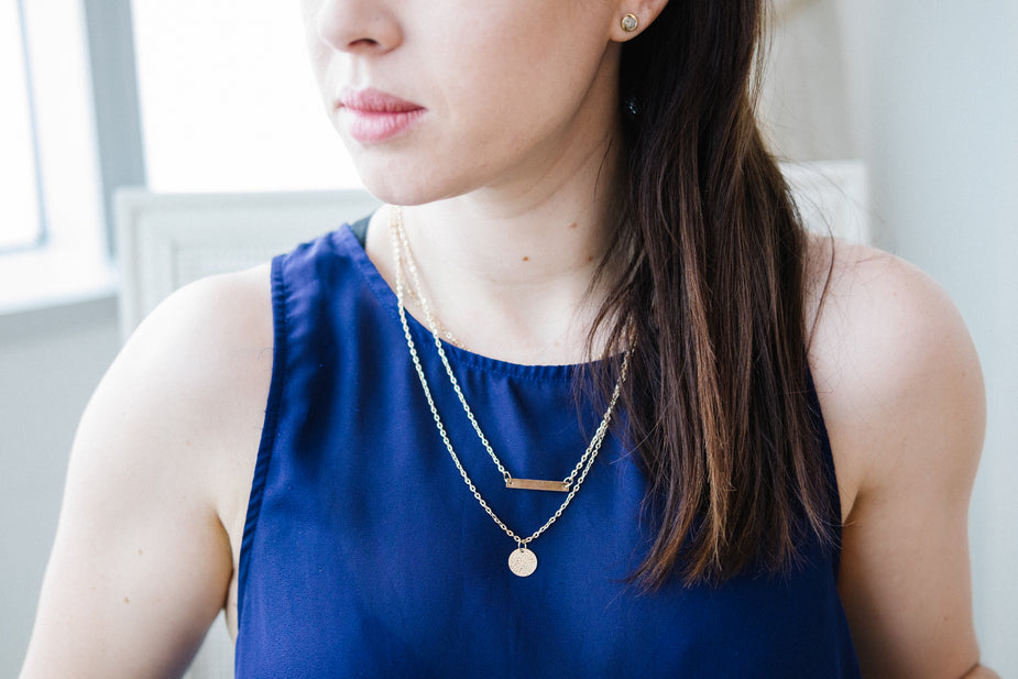 Woman wearing dainty gold necklace with layered chains and pendant, blue sleeveless top, casual jewelry style.