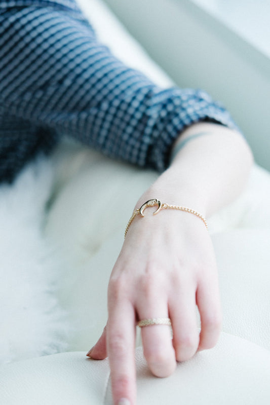 Moon Charm Bracelet in gold worn on woman's wrist with matching band ring