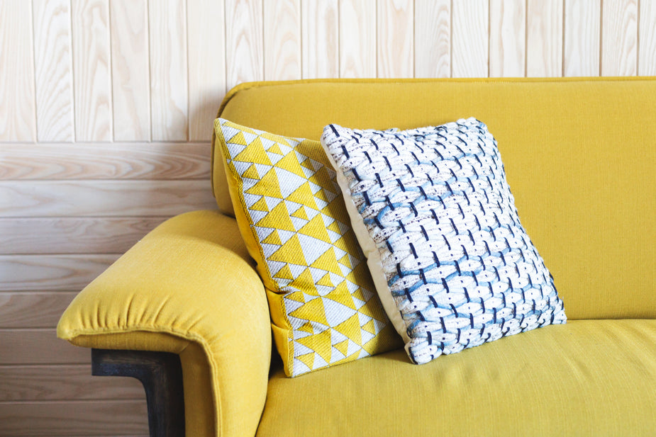 Yellow knitted throw pillows with geometric patterns displayed on a mustard yellow sofa against white shiplap wall.
