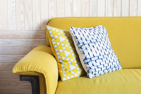 Yellow knitted throw pillows with geometric patterns displayed on a mustard yellow sofa against white shiplap wall.
