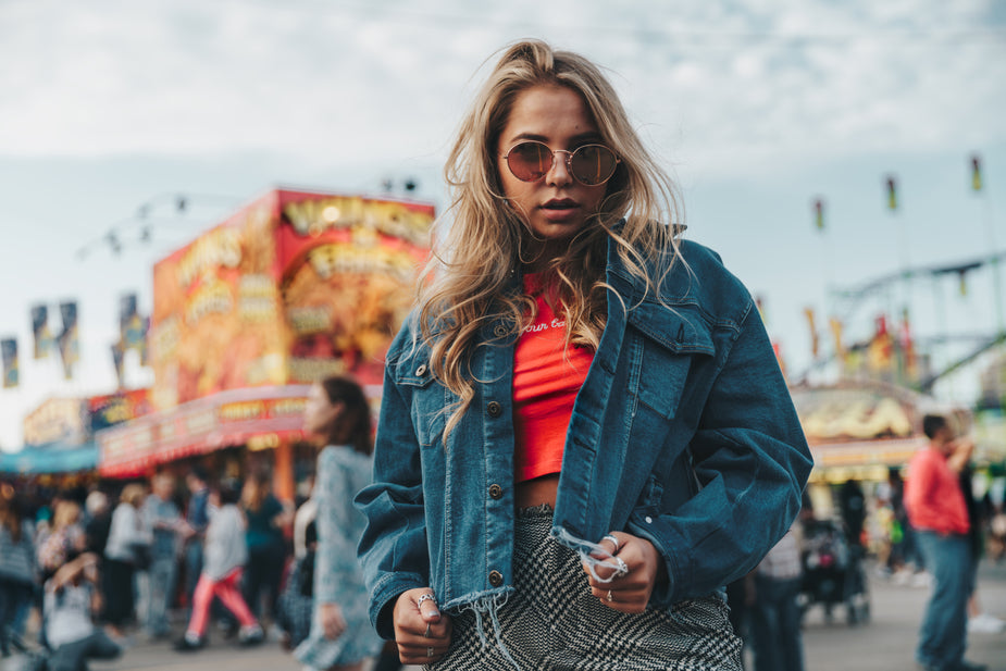 Woman wearing dark denim jacket with red top at fair, stylish casual outfit with sunglasses