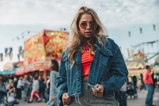 Woman wearing dark denim jacket with red top at fair, stylish casual outfit with sunglasses