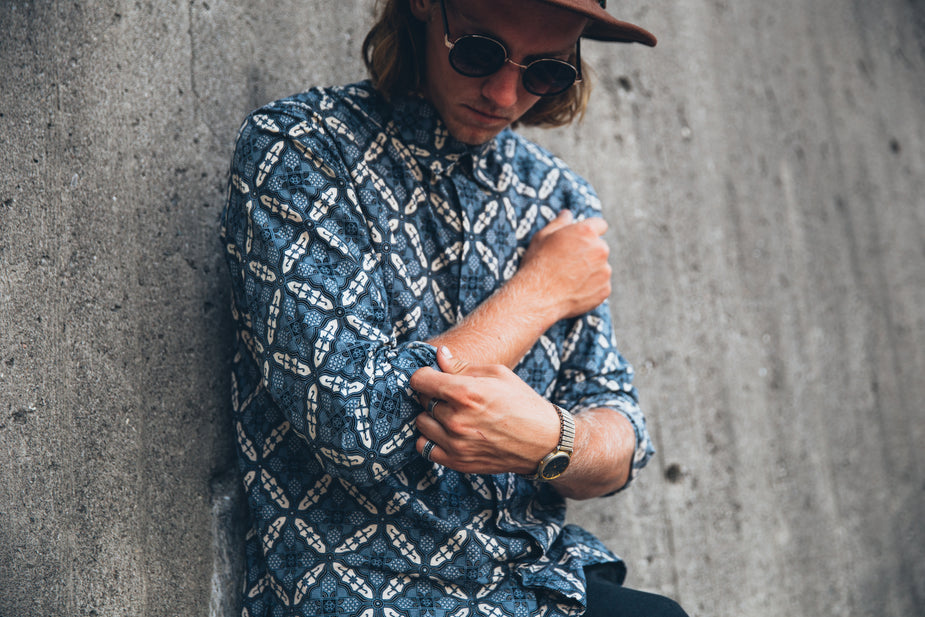 Ocean Blue Shirt with geometric pattern worn by man against concrete wall, styled with cap and sunglasses